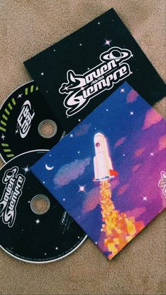 two cd's sitting on the floor next to each other, one with a space shuttle painted on it