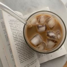 an open book next to a glass with ice on top and a straw in it