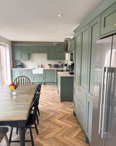 a kitchen with green cabinets and wood flooring next to a dining room table in front of a refrigerator