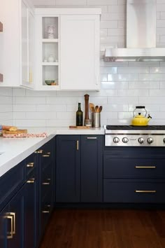 a kitchen with white and blue cabinets, wood flooring and brass pulls on the doors