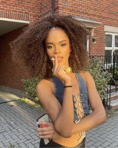 a woman standing outside eating an apple and looking at the camera with her finger in her mouth