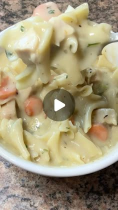 a white bowl filled with pasta and vegetables on top of a granite counter next to a spoon