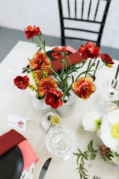 a white table topped with vases filled with red and yellow flowers