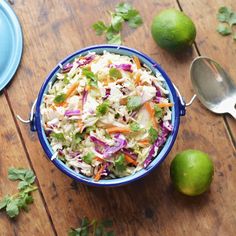 a blue bowl filled with coleslaw next to two limes on top of a wooden table