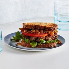 a sandwich with meat, tomatoes and lettuce on a plate next to a glass of water