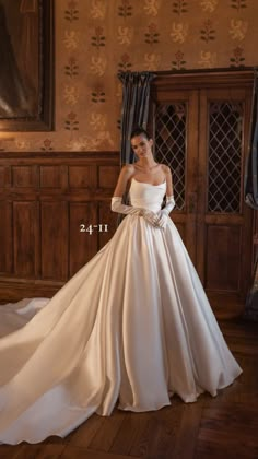 a woman in a white wedding dress standing on a wooden floor with her hands behind her back