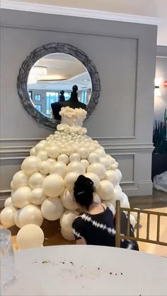 a woman sitting at a table in front of a giant cake made out of balloons