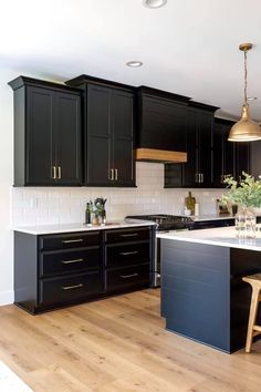 a large kitchen with black cabinets and white counter tops, wooden flooring and gold pendant lights