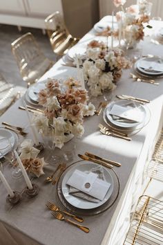 the table is set with white and gold place settings, silverware, and floral centerpieces