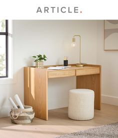 a wooden desk sitting next to a window on top of a hard wood floor in front of a white wall