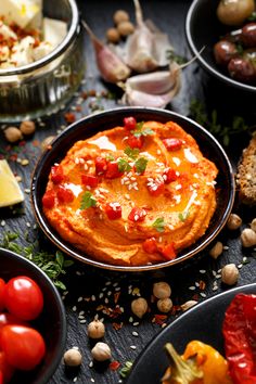 several different types of food in bowls on a table with bread, tomatoes and garlic