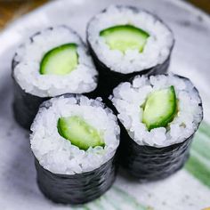 four sushi rolls with cucumber and white rice on a green striped plate