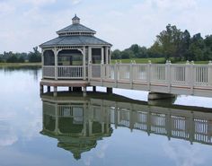 a white gazebo sitting on top of a lake next to a wooden bridge over water