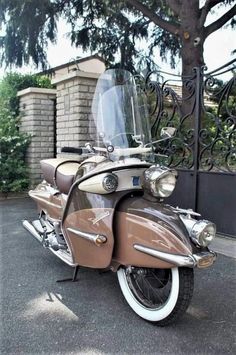 a brown and white motorcycle parked in front of a gated entrance to a house