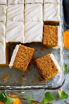 carrot cake with white frosting in a glass baking dish surrounded by flowers and leaves