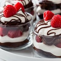 four desserts with chocolate, raspberries and whipped cream in small glass dishes