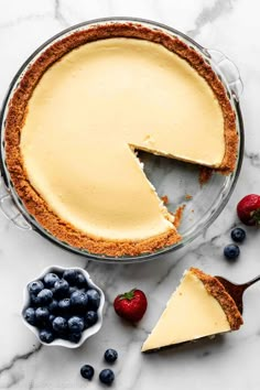 a cheesecake with a slice cut out and berries around it on a marble surface