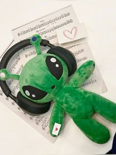 a green stuffed animal laying next to headphones on top of music sheets and envelopes