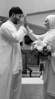 two people standing next to each other in front of a table with flowers on it