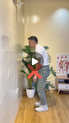 a man standing next to a potted plant on top of a hard wood floor