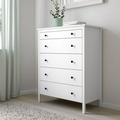 a white dresser with four drawers and a plant in the corner on top of it