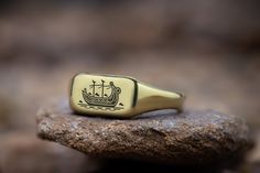 Set sail on a journey through time with our Viking Boat Engraved Rectangle Gold Ring. This meticulously crafted piece pays tribute to the adventurous spirit of the Vikings, featuring a detailed engraving of a Viking ship on a sleek rectangle-shaped gold band. Ideal for history buffs, mythology enthusiasts, or anyone inspired by the seafaring prowess and exploration of the Norsemen, this custom boat ring encapsulates the essence of Viking heritage. Made from premium gold, it's a bold expression o Rectangle Gold Ring, Viking Rings For Men, Viking Heritage, Viking Boat, Viking Rings, Dna Jewelry, Viking Ring, Viking Ship, Engraved Ring