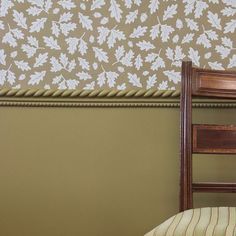 a wooden chair sitting in front of a wall with leaves on it's back