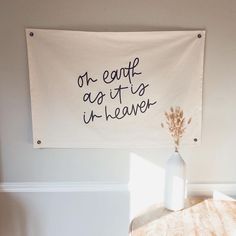 a white wall hanging above a table with a vase on it and a sign that says, oh eaaff ag tis un leaver