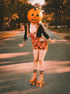 a woman in an orange dress is rollerblading with a pumpkin on her head