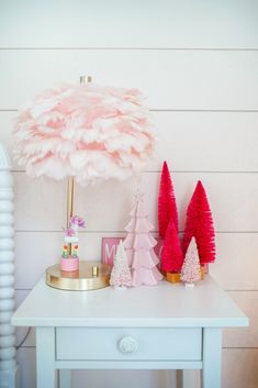 a white table topped with pink christmas trees and a pink feather lamp on top of it