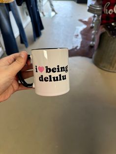 a person holding a coffee mug with the words i love being delluu on it