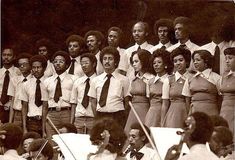 a group of people standing next to each other in front of orchestra instruments and conductor