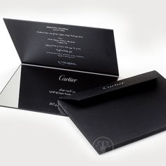 an open black card and envelope on a white background with the word cartier written in cursive writing