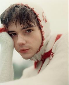 a young man wearing a white and red sweater holding his hand to his face while looking at the camera