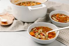 two white bowls filled with soup on top of a cloth next to a pot and spoon