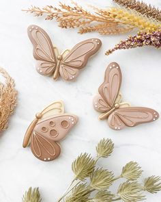 three butterfly shaped cookies sitting on top of a white marble table next to dried flowers