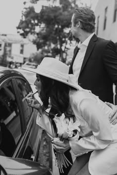 a man in a suit and tie standing next to a woman who is leaning on a car