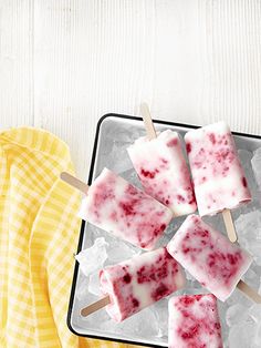 four popsicles with raspberry toppings on a tray next to a yellow towel