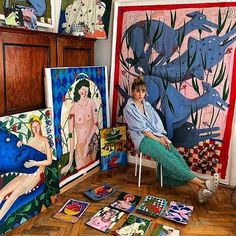 a woman sitting on a chair in front of some paintings and cards that are laying on the floor