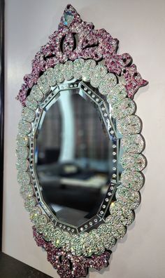 an ornate mirror with pink and green crystals on the bottom is hanging on a wall