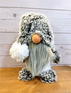 a stuffed animal is sitting on a wooden table and wearing a hat with pom poms