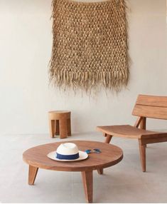 two wooden chairs and a table with a hat on it in front of a woven wall hanging