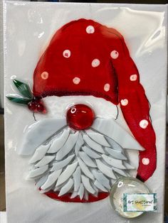 a red santa hat with white feathers and a green berry on the side, sitting on top of a piece of paper