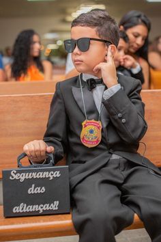 a young boy sitting on top of a wooden bench wearing sunglasses and holding a bag