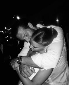 a man and woman hugging each other in black and white photo with lights behind them