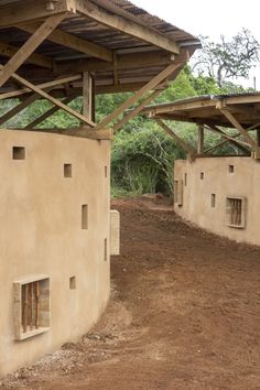 an adobe building with several windows on the side and one in the middle, under a wooden roof