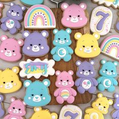 decorated cookies with teddy bears and rainbows are on a wooden table next to a cupcake