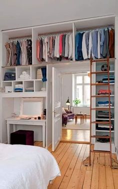 an open closet with clothes on shelves and a ladder in the middle, next to a bed