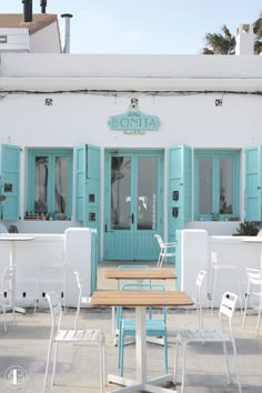 tables and chairs in front of a building with blue shutters on the doors,