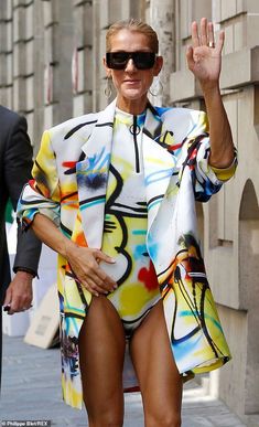 a woman in a colorful swimsuit waves to the crowd as she walks down a city street